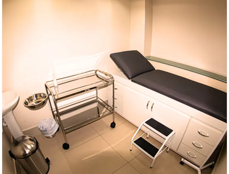 Sala de procedimentos de enfermagem com maca e carro de materiais